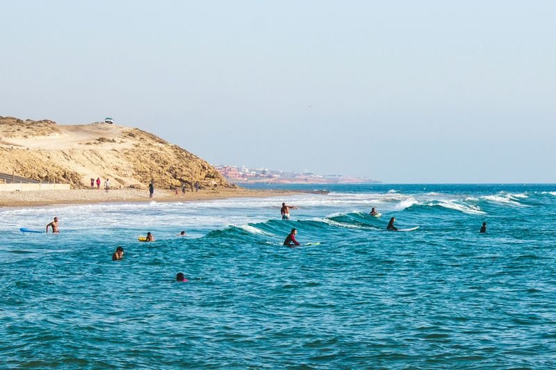 Principiantes en la espuma en la playa de Tamraght, con el cabo detrás