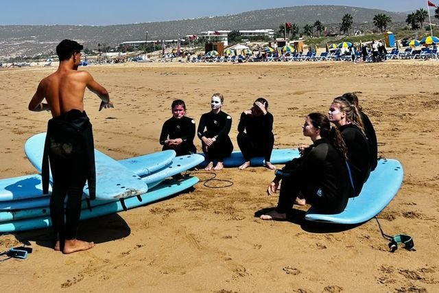 Ein Coach gibt Anfängern, die neben ihren Boards im Sand sitzen, eine Einweisung