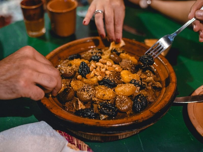 Eine Tajine mit Fleisch, Pflaumen und Mandeln, am Tisch geteilt