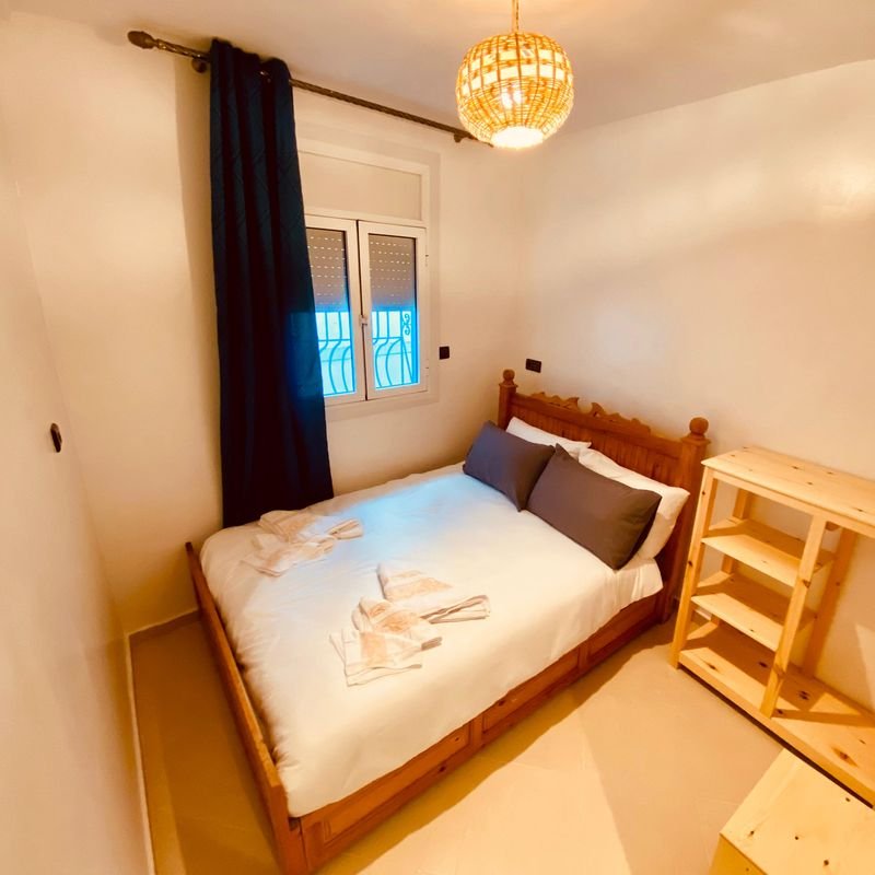 Double room at the Taghazout hostel: a double bed with folded towels, dark curtains and a wooden shelf unit