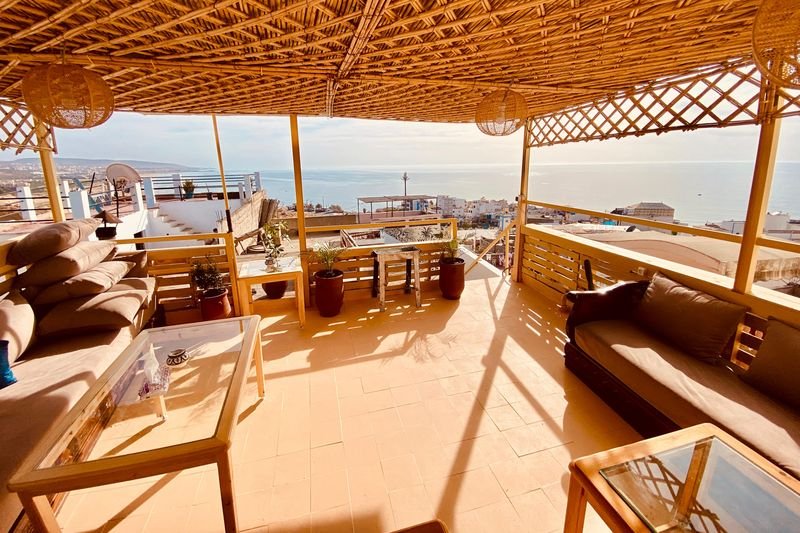 La terrasse sur le toit de notre hostel de Taghazout : canapés sous la pergola en roseau, le village et l'Atlantique derrière