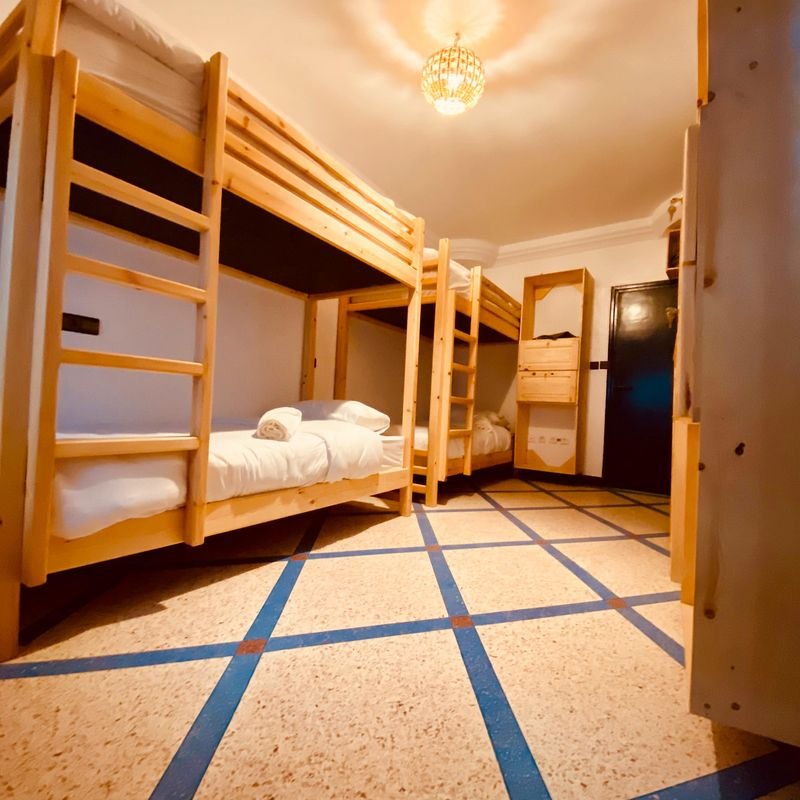Mixed dorm at the Taghazout hostel: pine bunk beds along a tiled corridor with a blue border