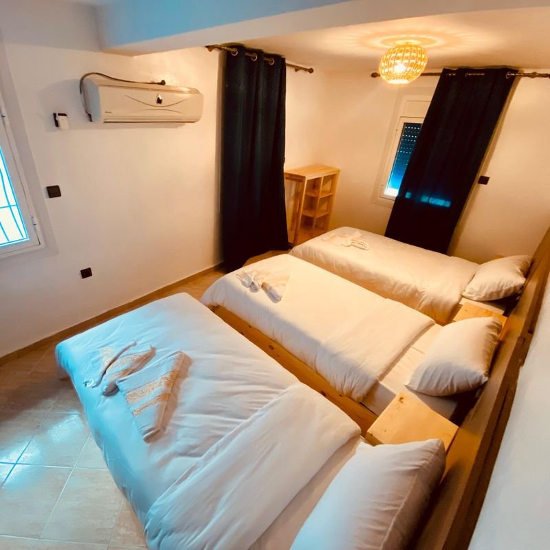 Triple room at the Taghazout hostel: three single beds side by side under a pendant lamp