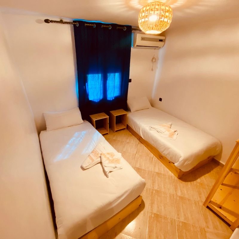 Twin room at the Taghazout hostel: two single beds, bedside tables and an air-conditioning unit above the window