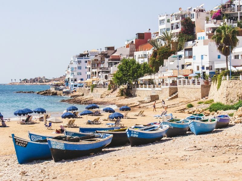 Taghazout beach: blue fishing boats hauled onto the sand, the white village climbing the slope behind