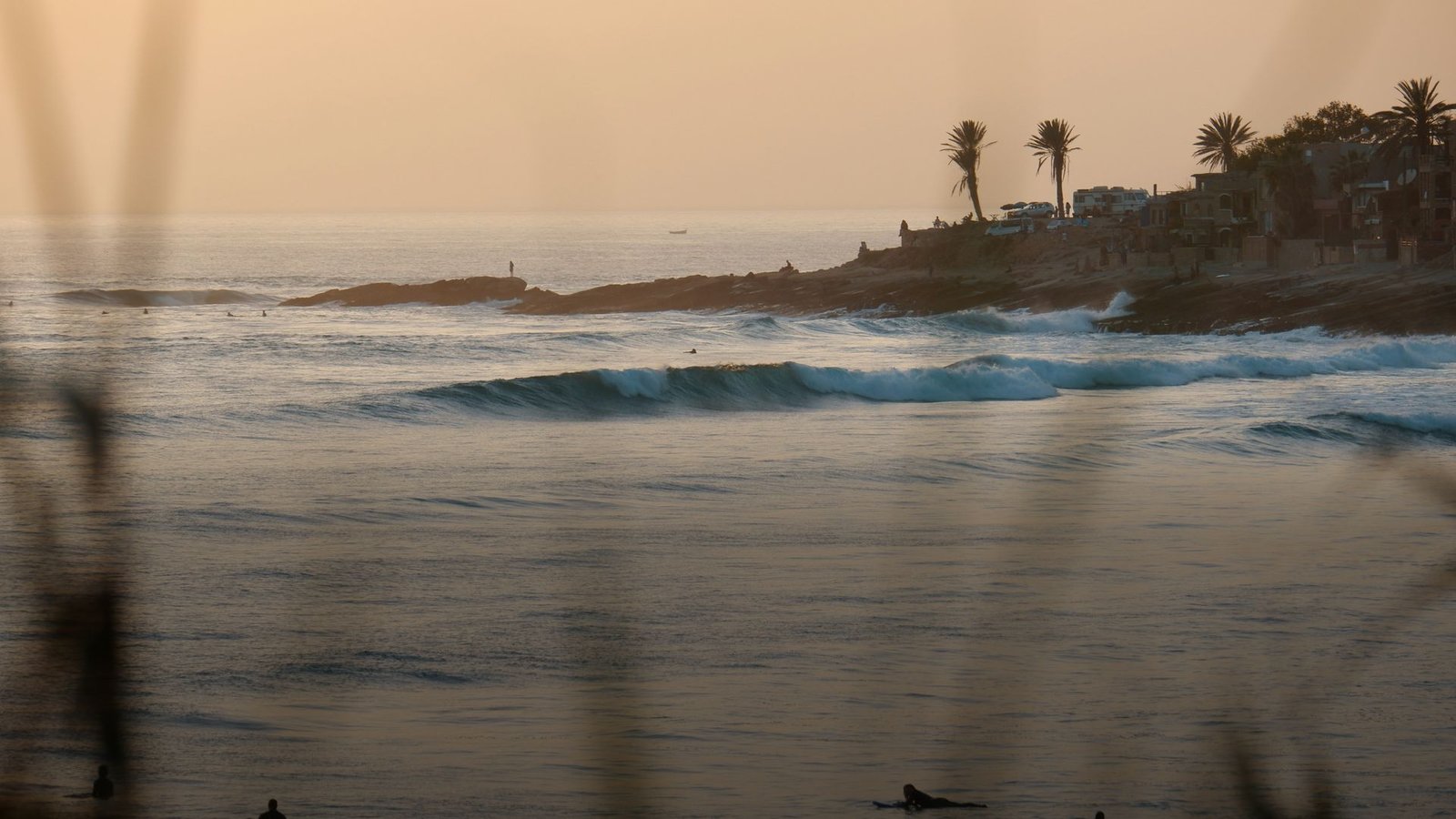 Surfer warten in Taghazout auf die letzten Wellen des Tages, Palmen und Dächer auf der Landspitze