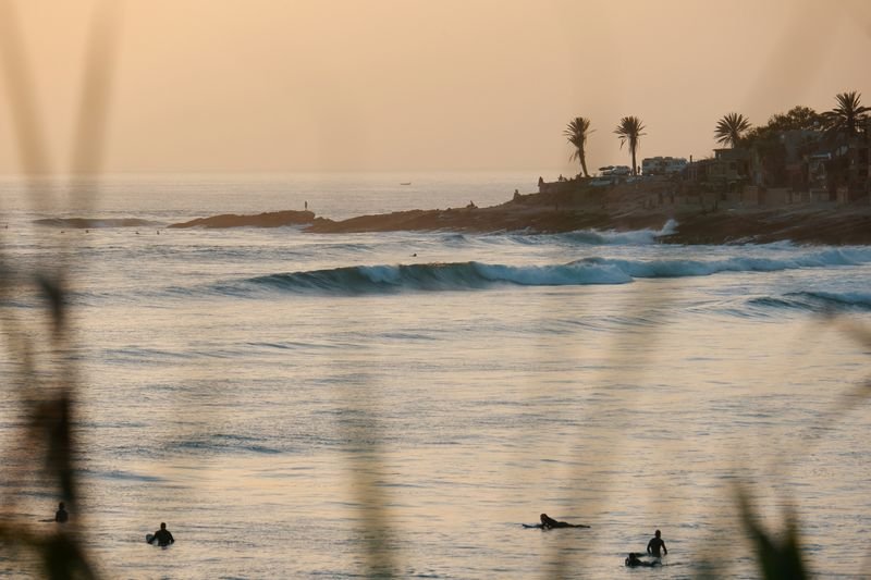Surfers waiting for the last waves of the day at Taghazout, palms and rooftops on the point