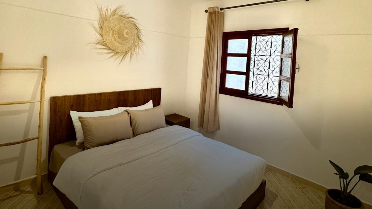 Habitación doble del hostel de Tamraght: cama doble hecha, un tapiz trenzado en la pared y una ventana con celosía