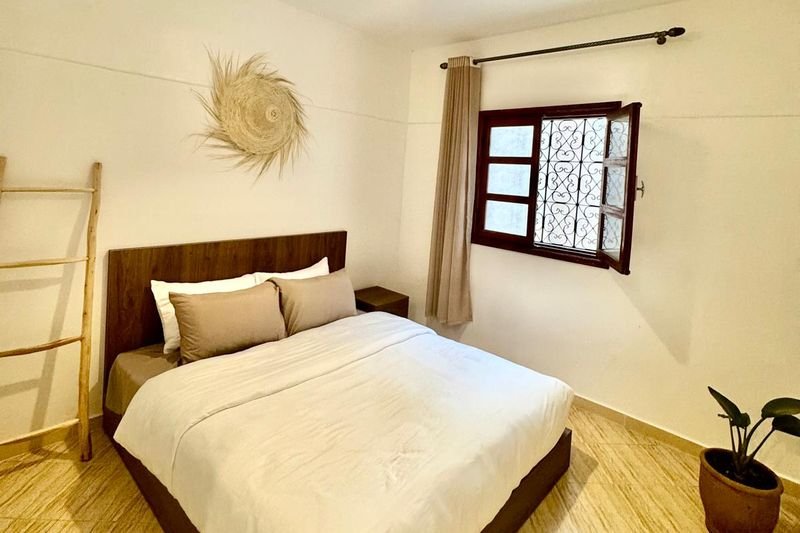 Habitación doble del hostel de Tamraght: cama doble hecha, un tapiz trenzado en la pared y una ventana con celosía