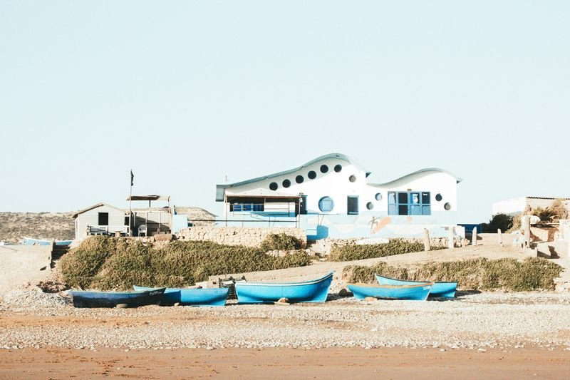 Blaue Boote und weiße Häuser am Strand von Tamraght unter klarem Himmel
