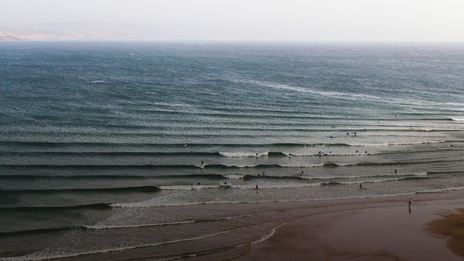 Swell-Linien laufen in die Bucht von Imsouane, ein einzelner Surfer im Wasser